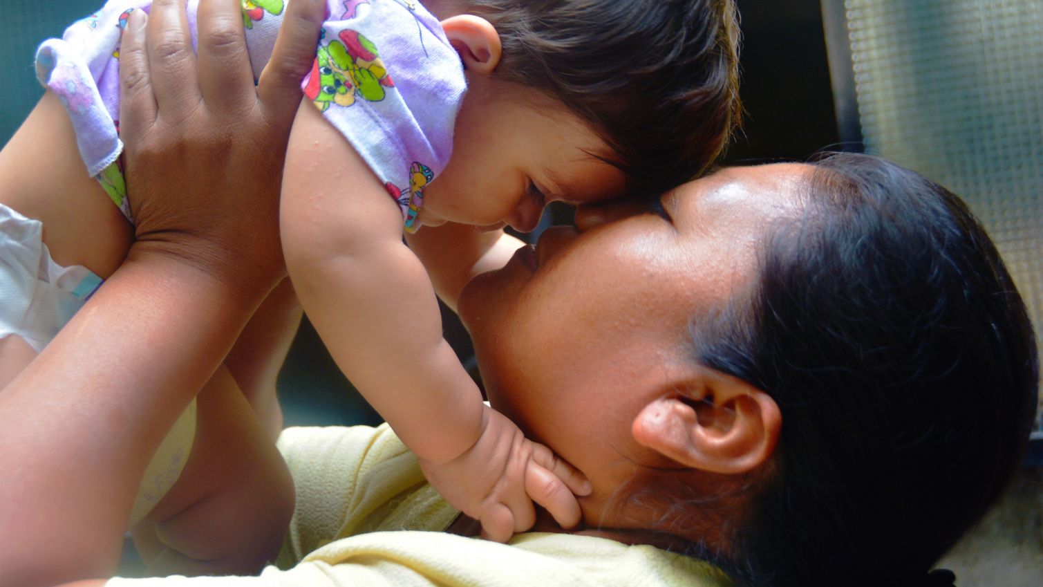 Adult holding child in air while kissing them.
